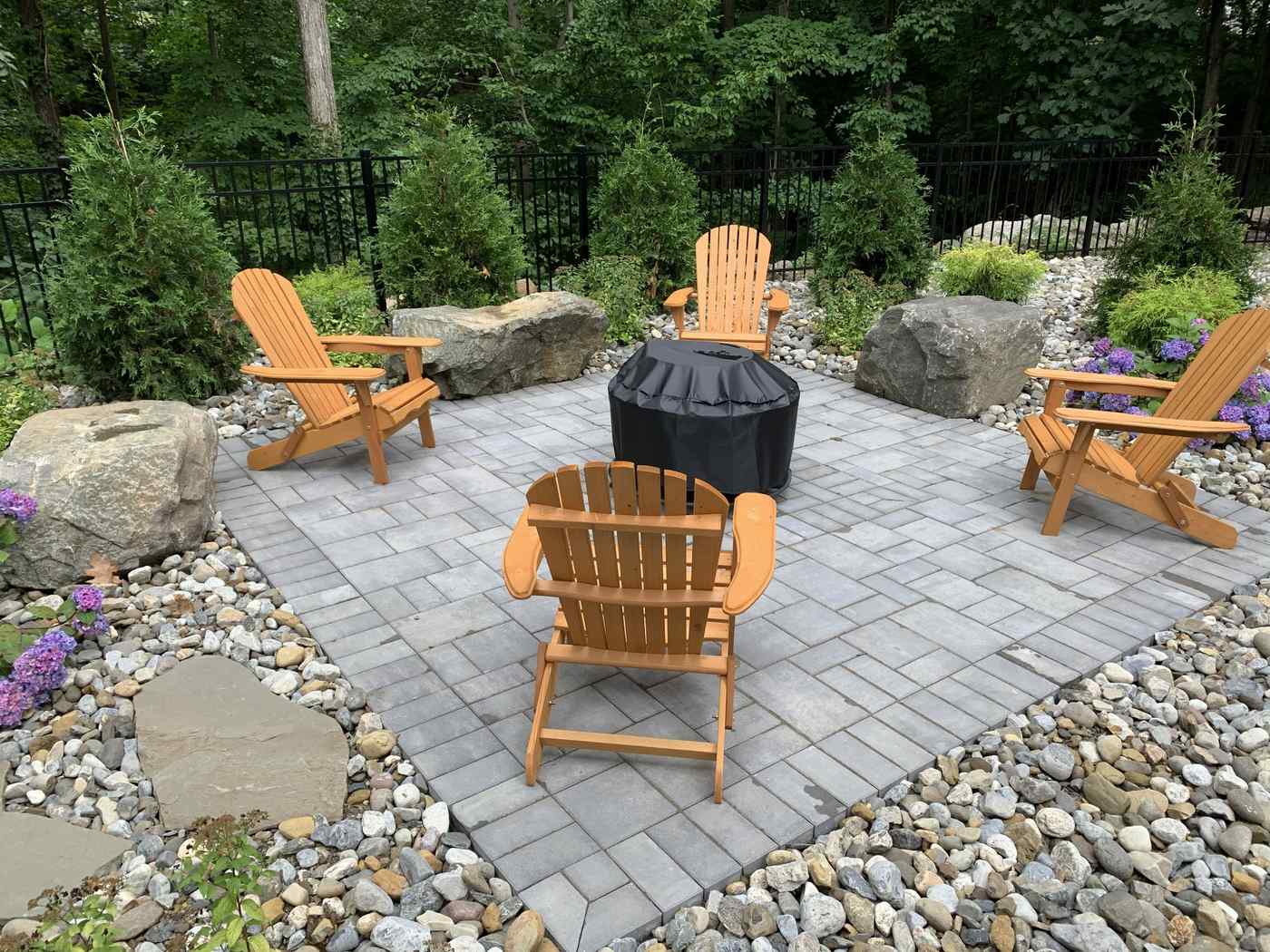 Custom paver fire pit patio with Adirondack chairs and river rock landscaping in Ringwood NJ