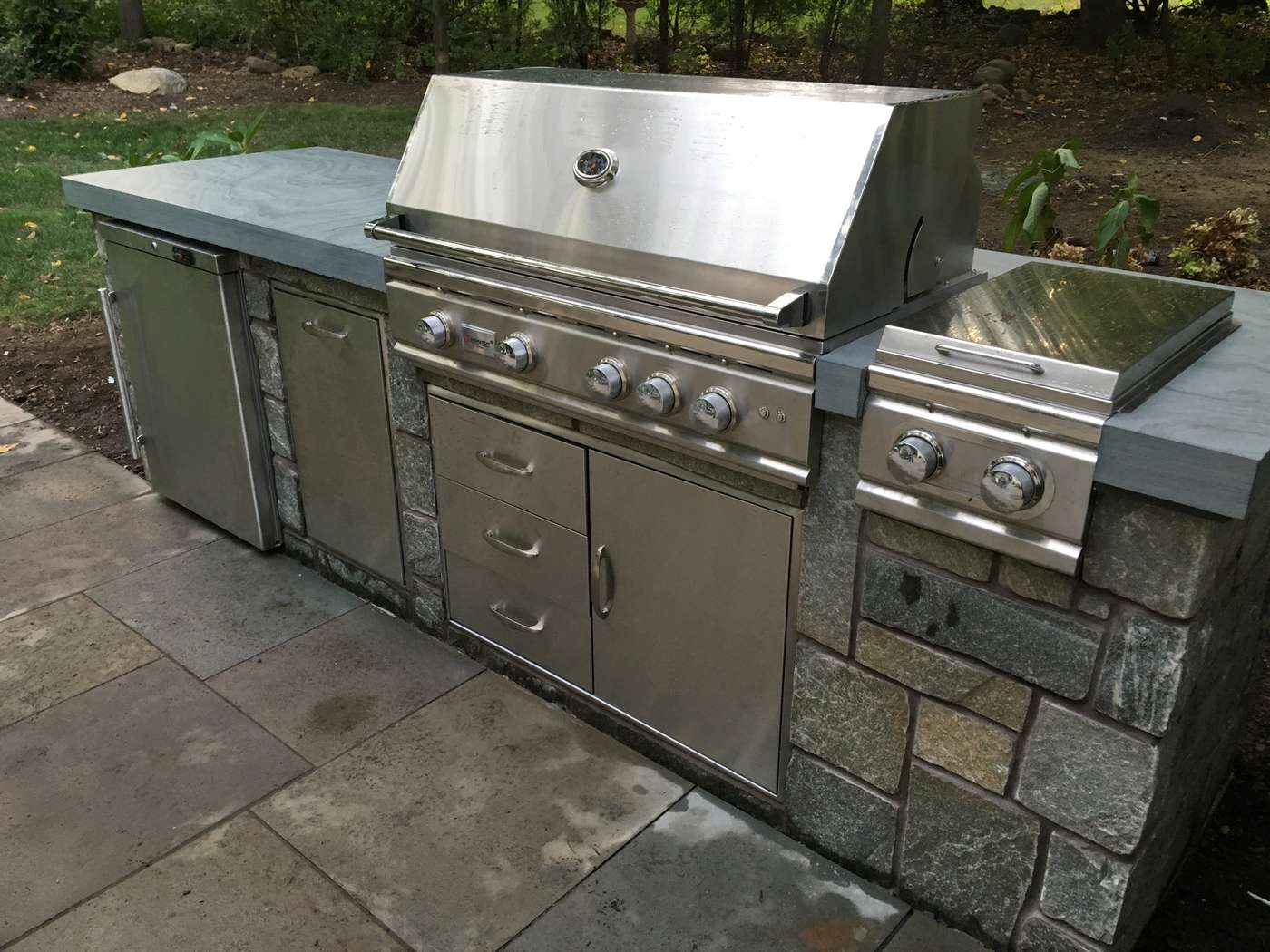 Custom fieldstone outdoor kitchen with built-in stainless grill, side burner, and refrigerator in Ringwood NJ