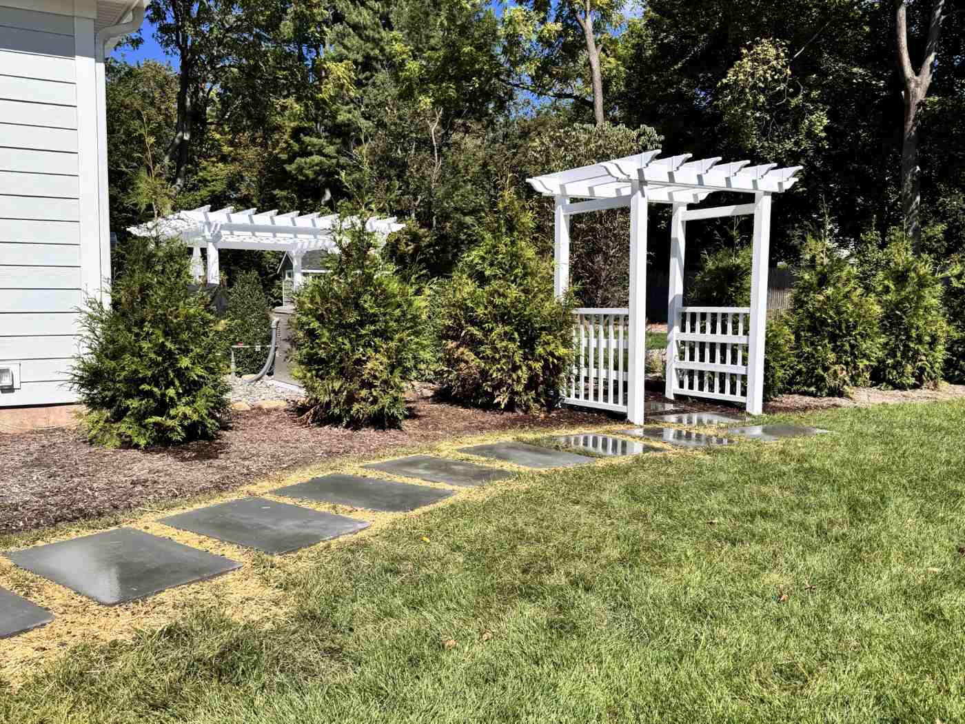 Matching white vinyl garden arbors and pergola structures with bluestone walkways in Ringwood NJ